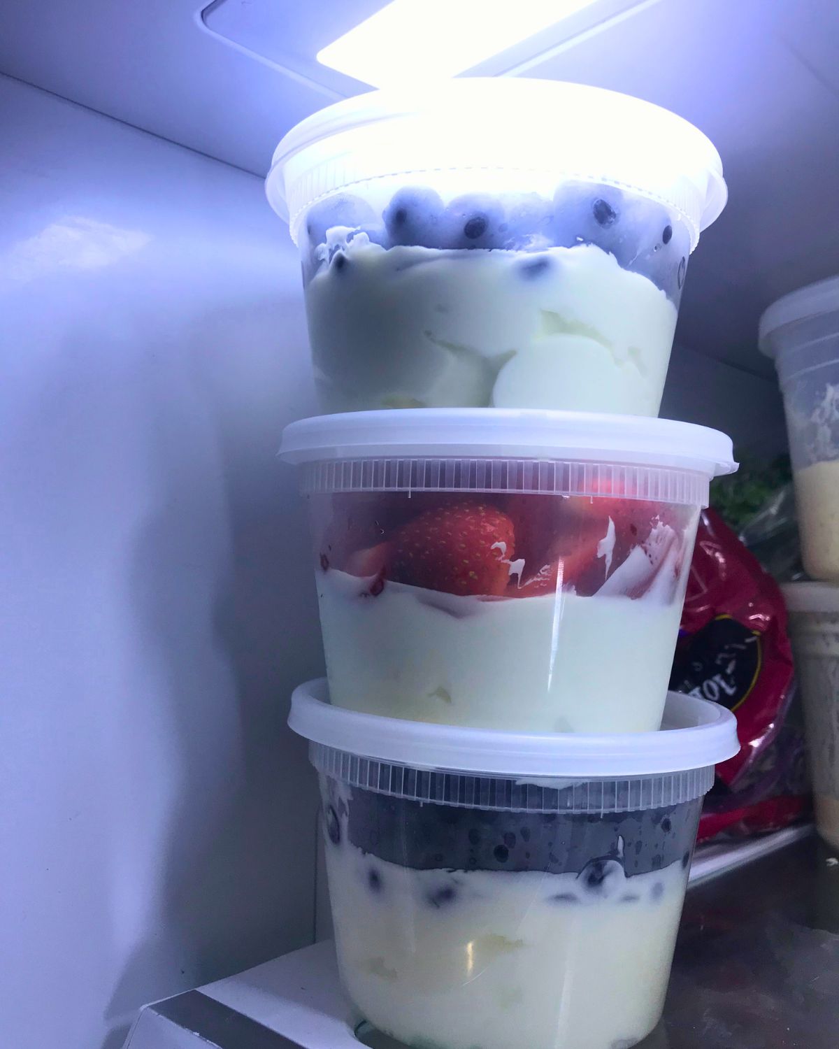 stacked tubs of greek yogurt and fruit in the fridge.