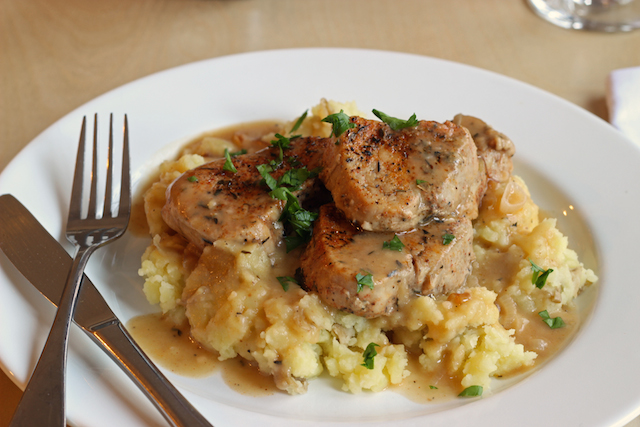 A plate of Pork, gravy, and mashed potatoes