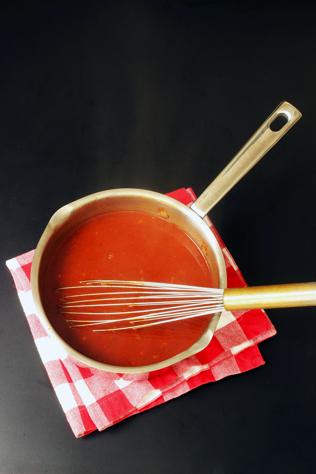 red enchilada sauce in a pot with a whisk next to red checked napkin
