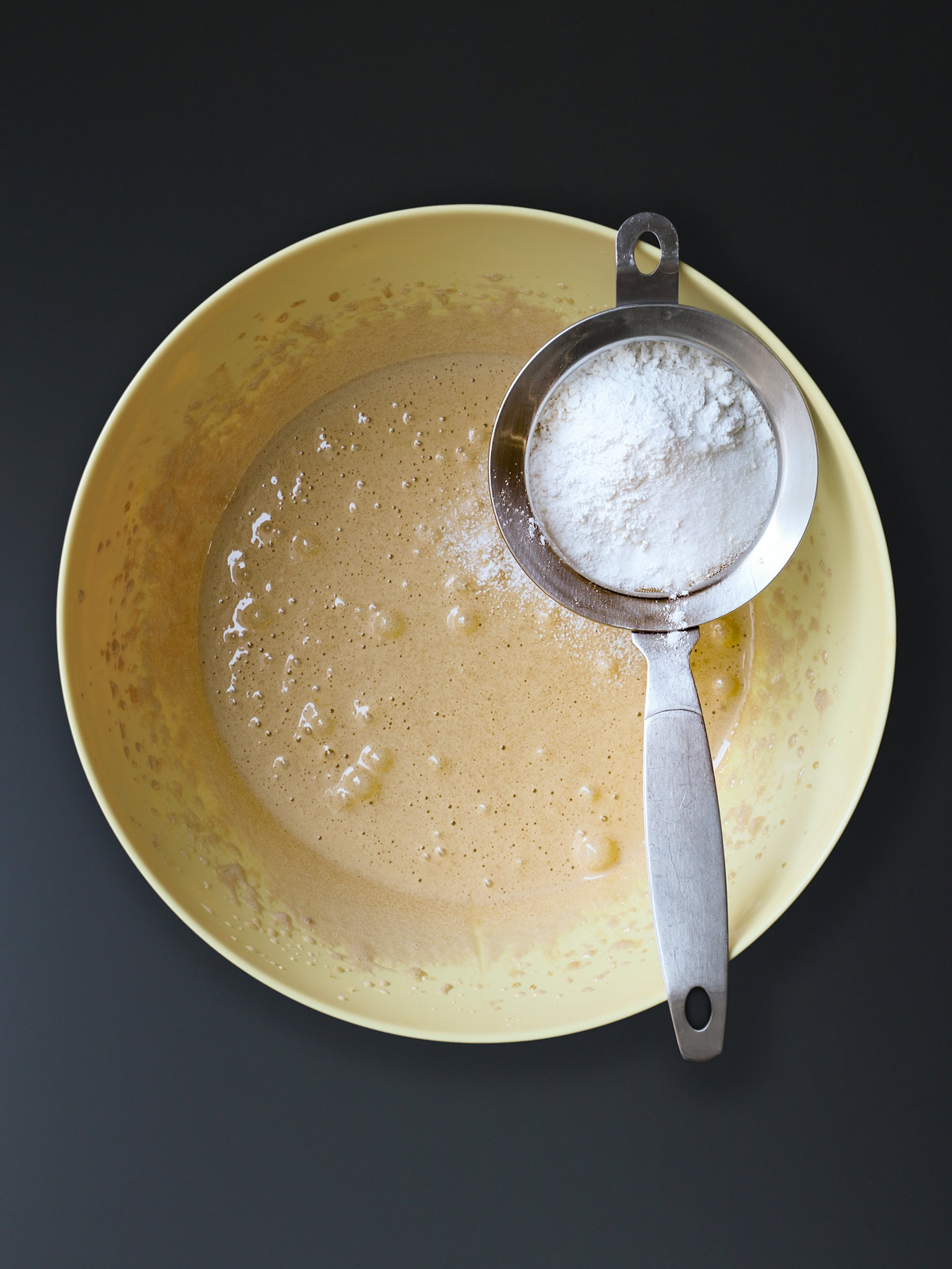 sifter over yellow bowl of egg and sugar mixture.