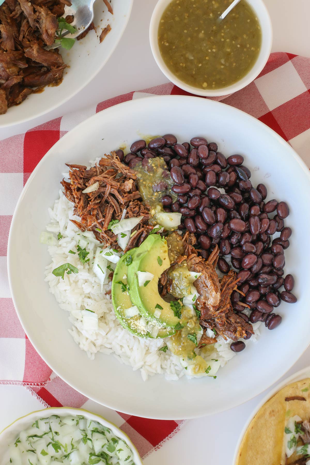 rice bowl topped with shredded beef, black beans, salsa verde, and avocado.