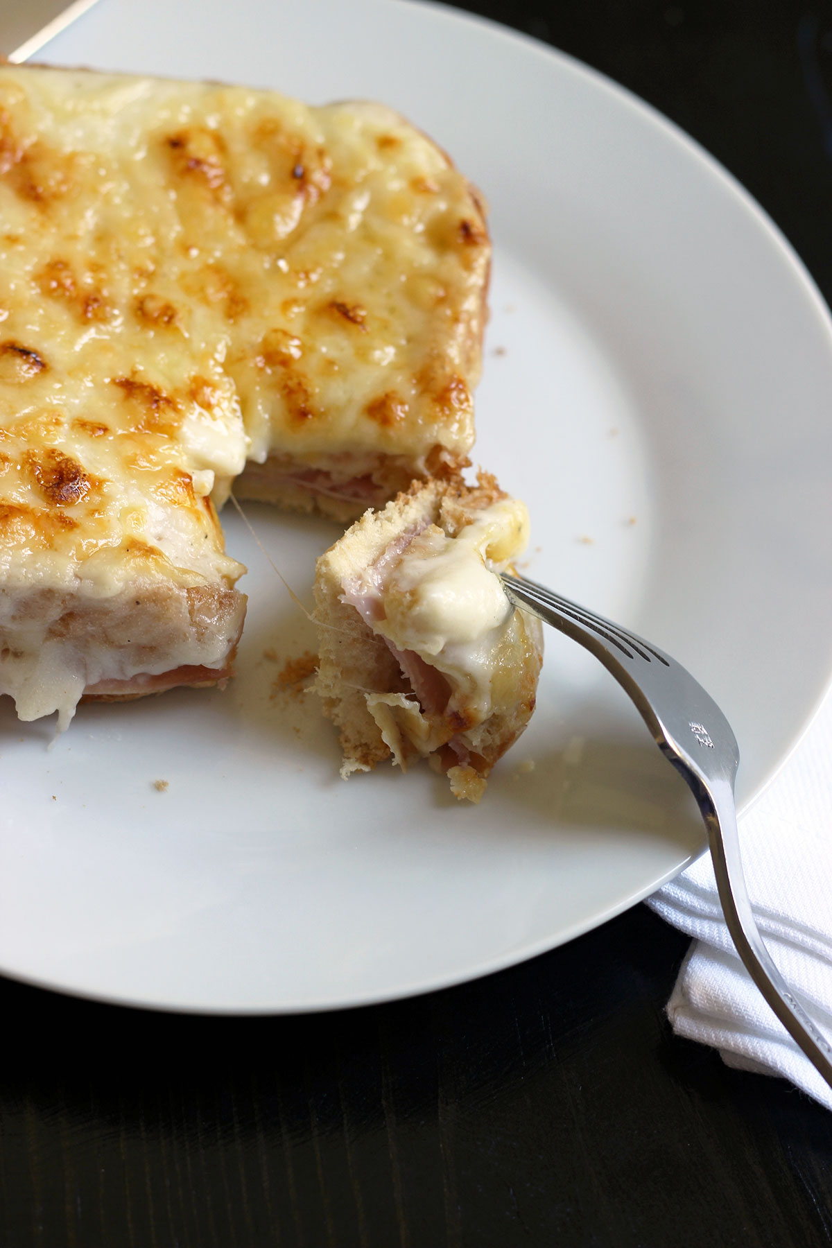 sandwich on plate with bite of croque monsieur with bechamel on fork.