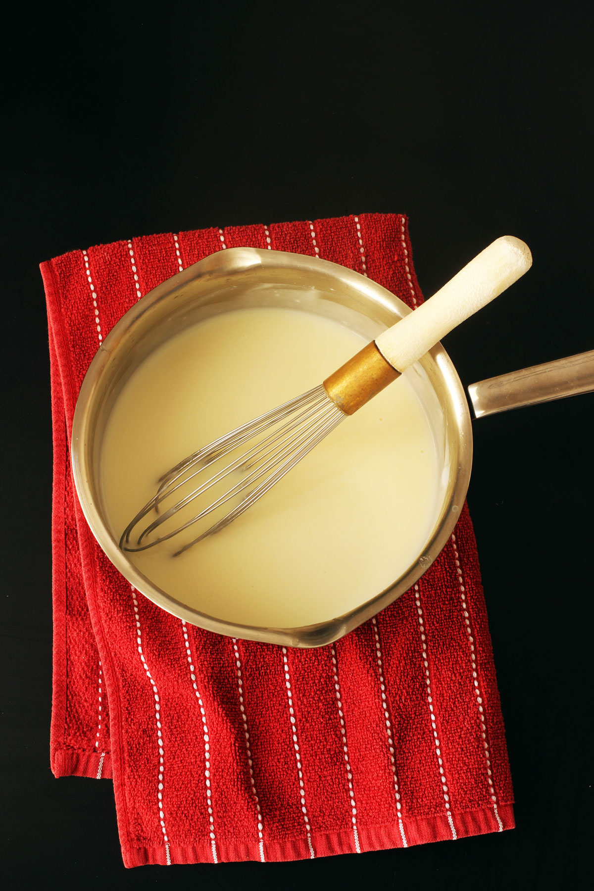 white sauce or bechamel in pot with whisk atop a red striped towel.