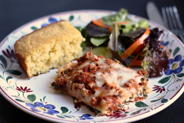 slice of lasagna on a plate with cornbread and salad