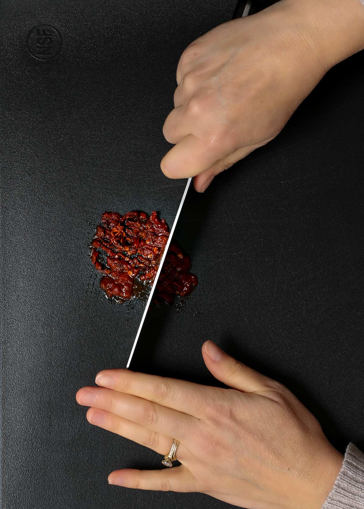 chopping chipotle peppers on a black cutting board.