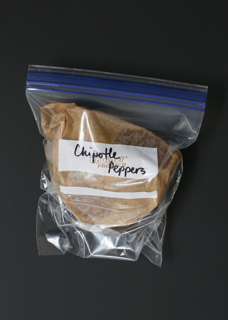 ziptop bag labeled with the words chipotle peppers, inside is the folded parchment with the frozen chiles inside.