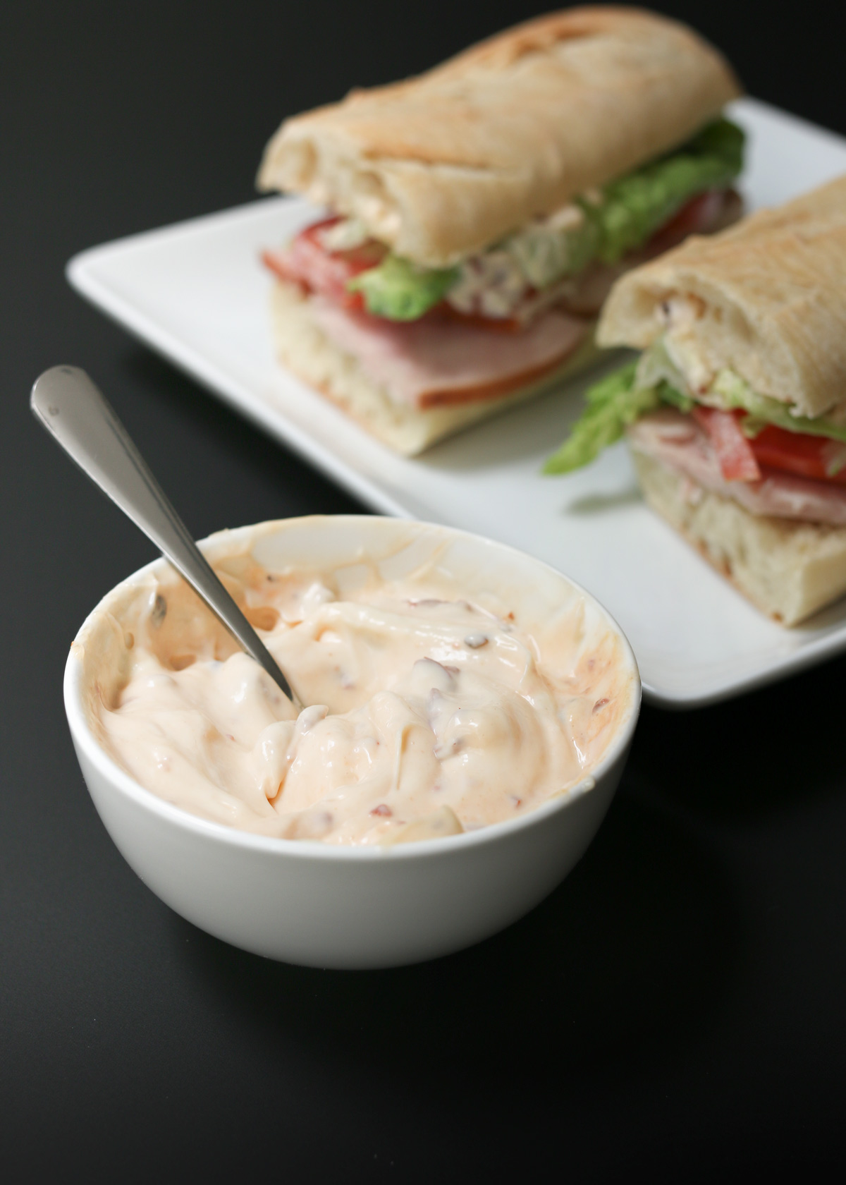 bowl of chipotle mayonnaise near a plate of sandwiches.