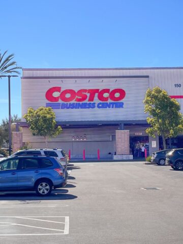 costco business sign on front of building with parking in foreground, a palm tree against blue sky is to the side.