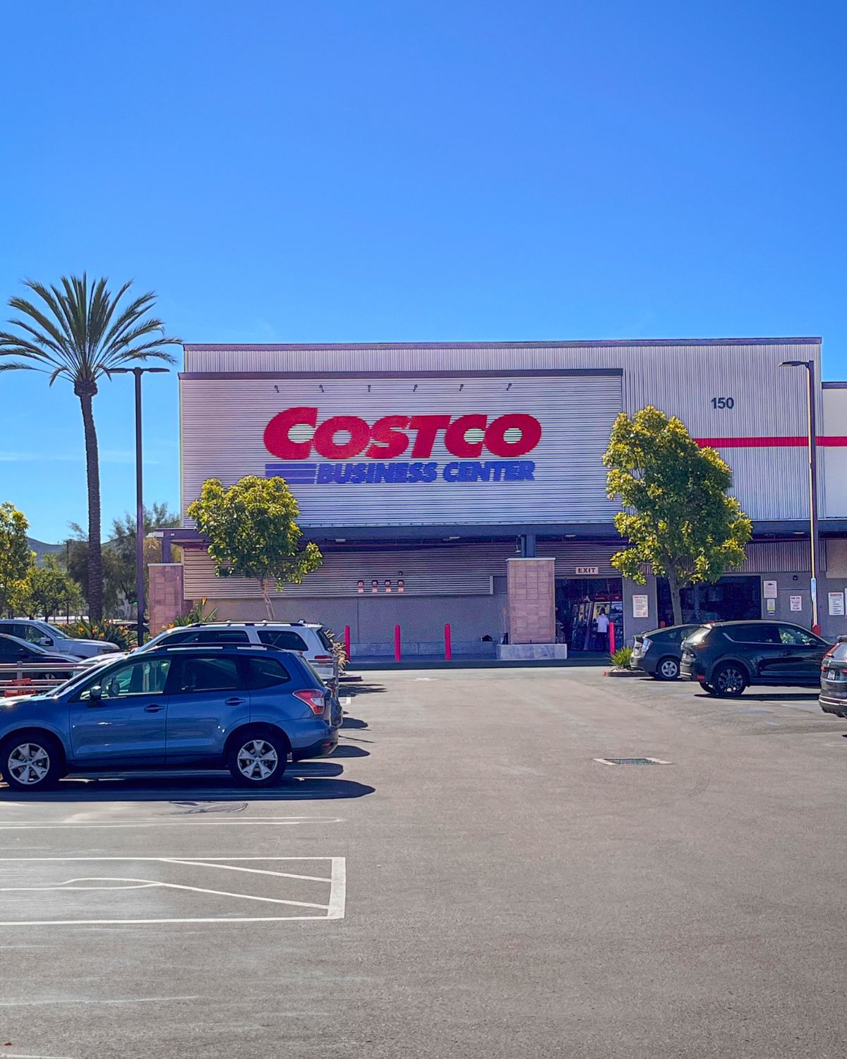 frontage of Costco business on a sunny day with blue skies, cars in parking lot.