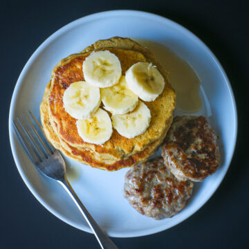 overhead shot of pancake stack topped with banana slices next to sausage patties.