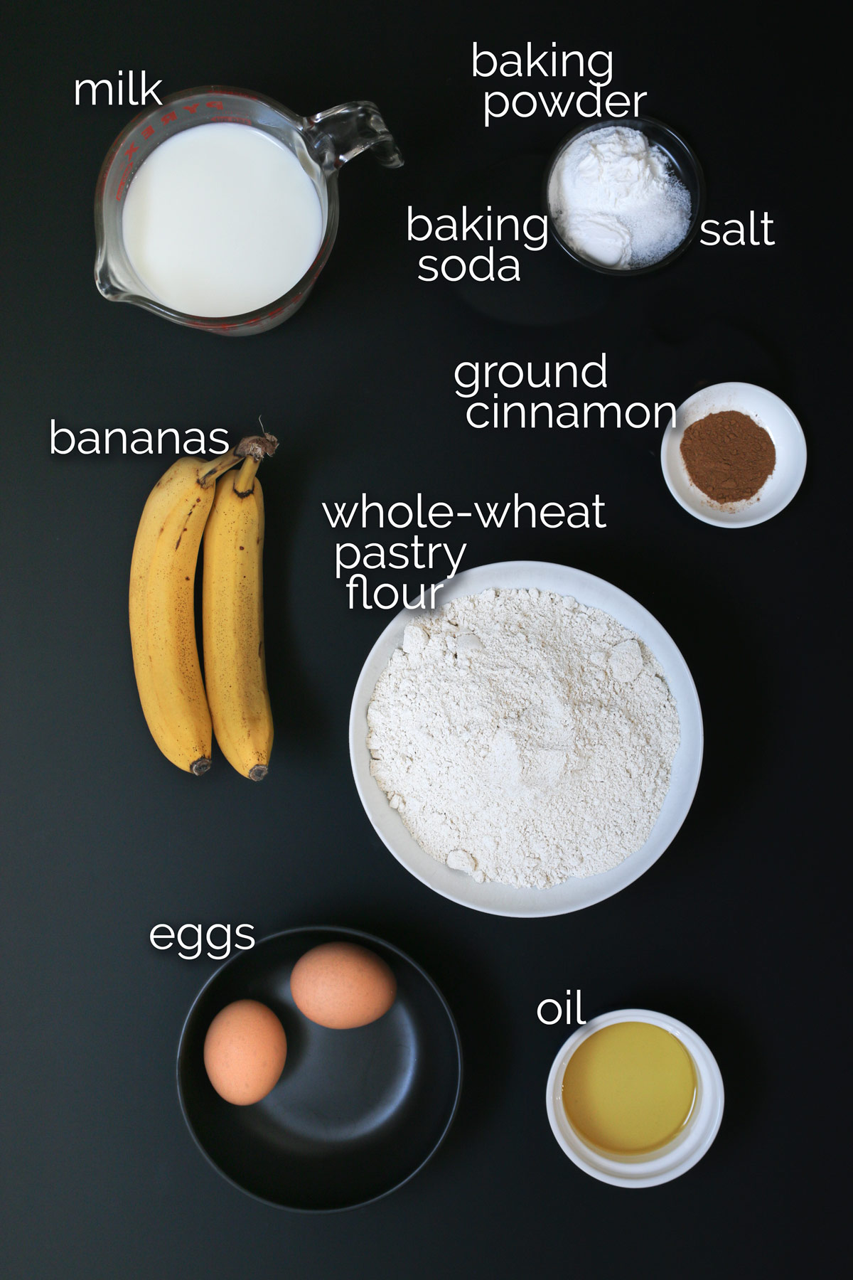 ingredients for banana whole wheat pancakes laid out on black table top.