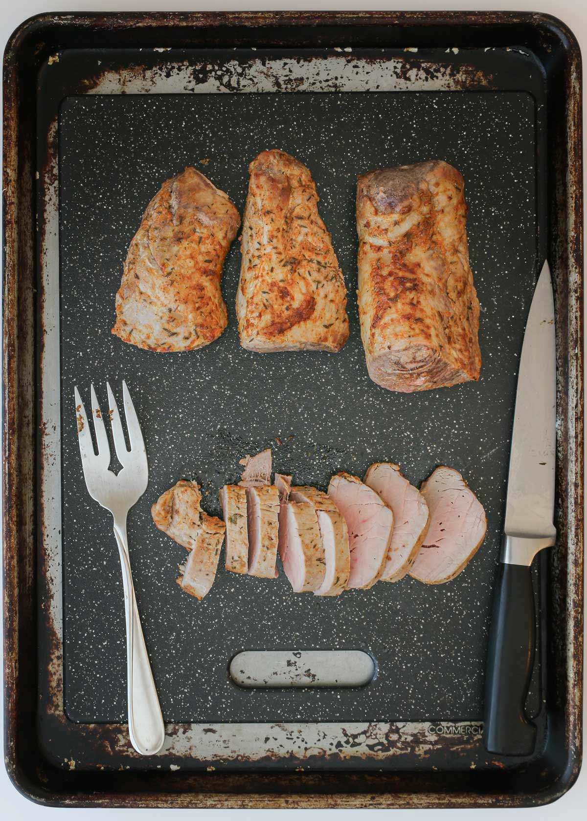 sliced pork tenderloin on black cutting board on a baking sheet to catch the drips.