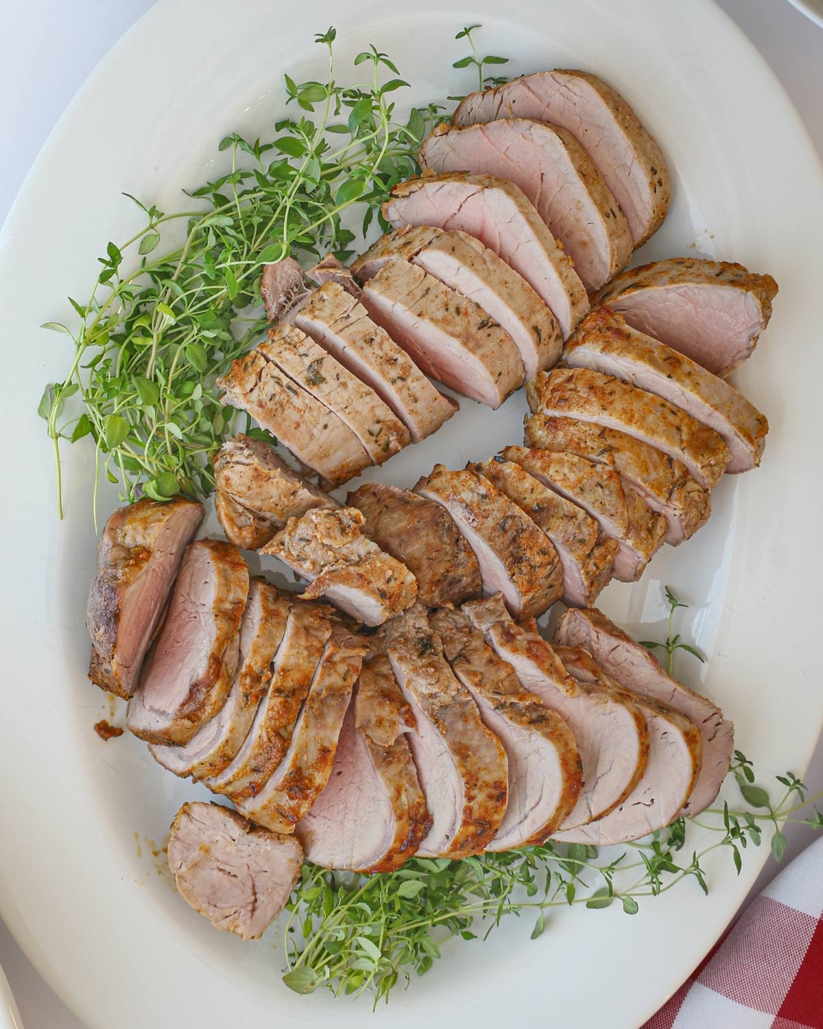 air fryer pork tenderloin sliced and laid out on a platter with fresh thyme.