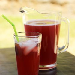 pitcher of cherry limeade with glass and limes