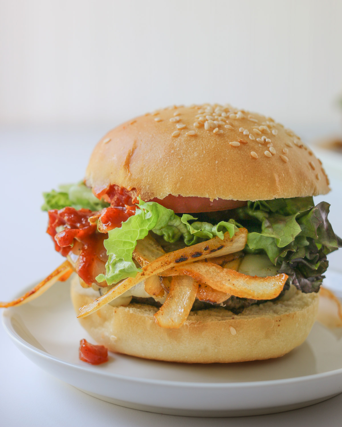 BBQ Bacon Burger with sauce dripping onto plate, in front of a white background.