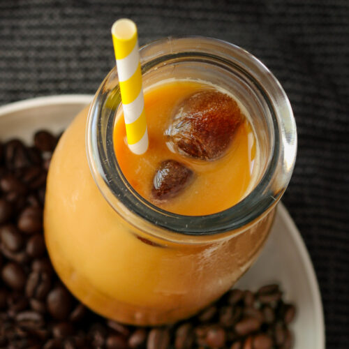 iced coffee in milk bottle, surrounded by coffee beans.