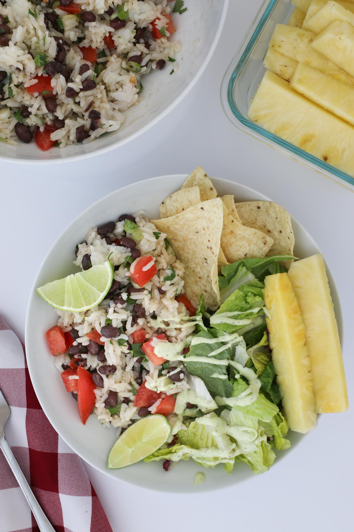overhead shot of plate of rice and black bean salad next to a green salad, tortilla chips, and pineapple spears.
