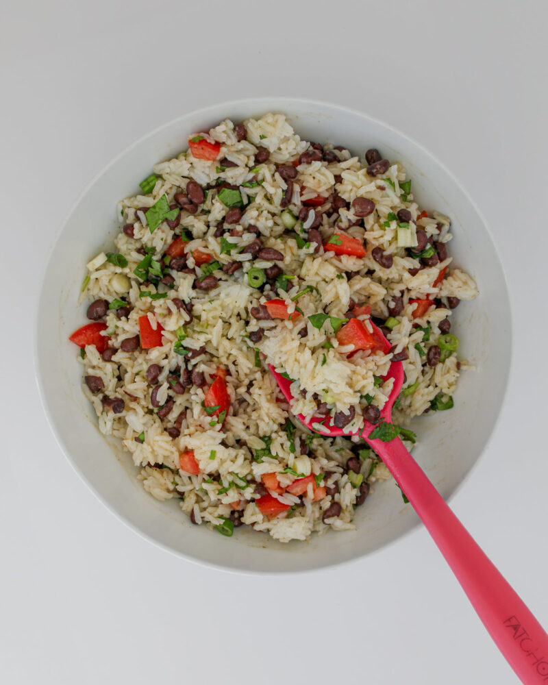 the mixed black bean and rice salad in a white bowl with a red spatula.