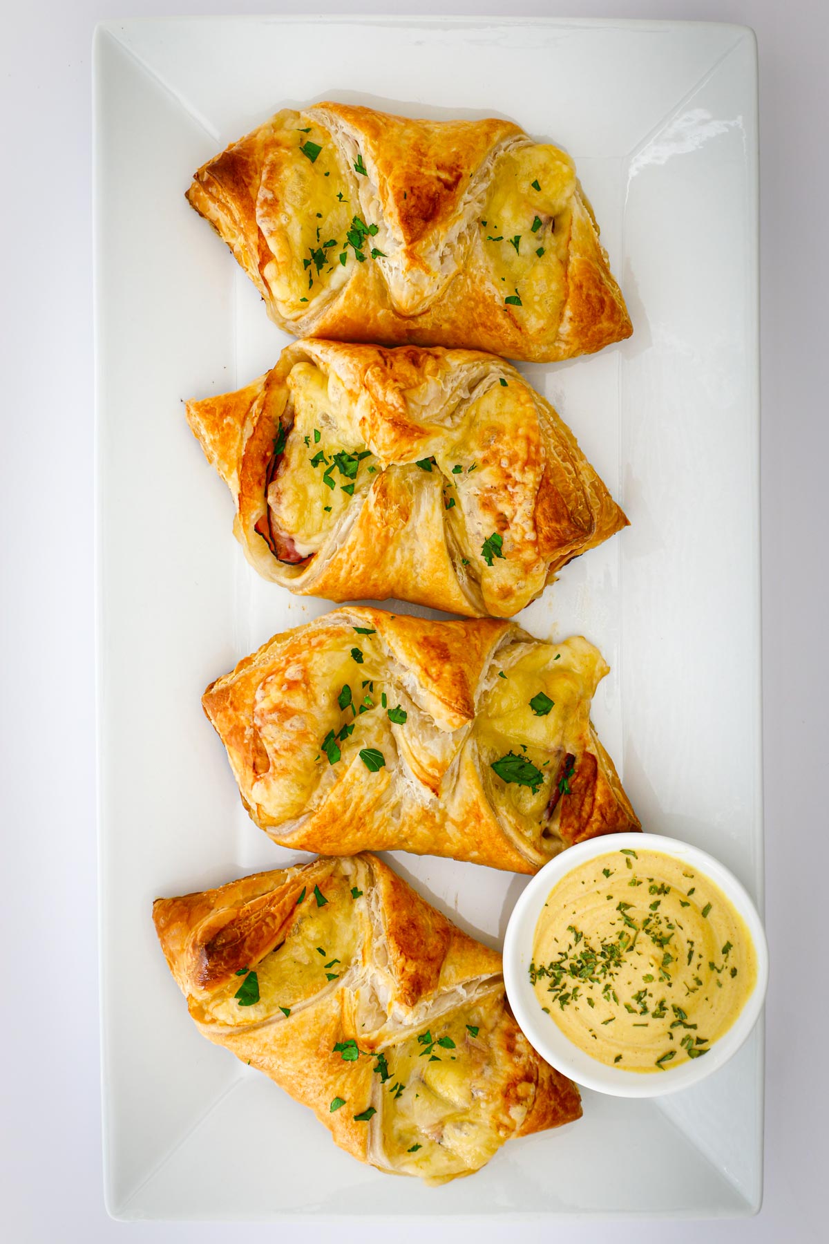 overhead shot of four ham and cheese croissants on a white tray with a dipping sauce.