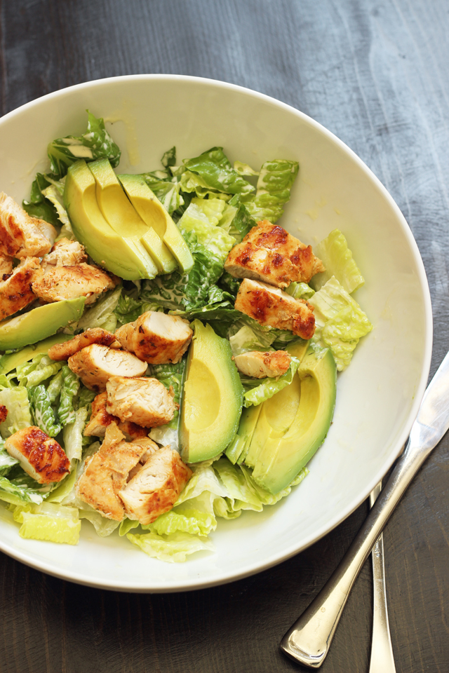 caesar salad topped with avocado and chicken.