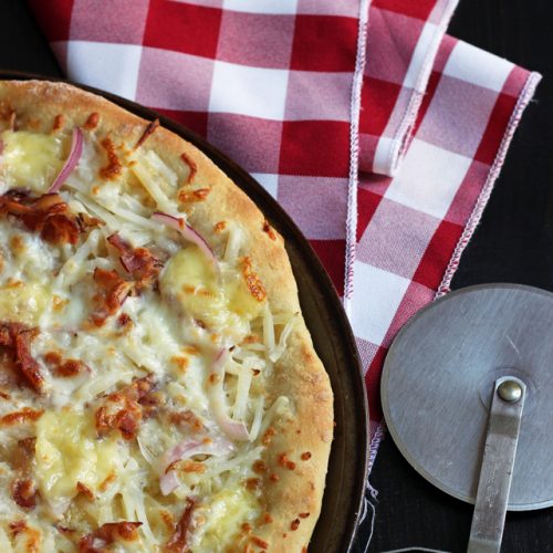 Tartiflette Pizza on table with pizza cutter