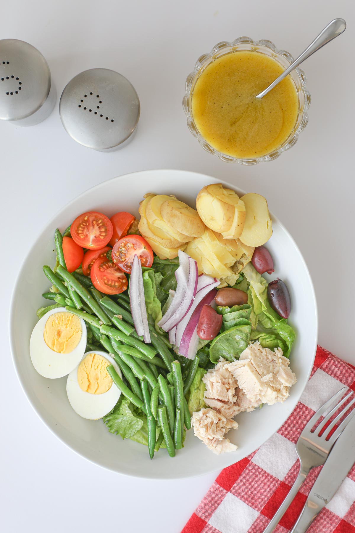 overhead shot of salade nicoise with tuna on table with napkin and cutlery and dish of vinaigrette.