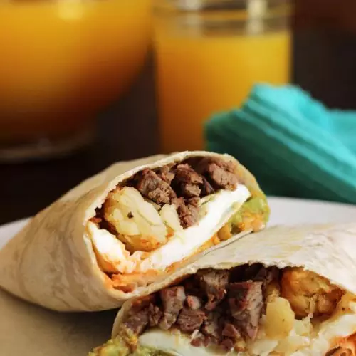 breakfast burrito cut in half, pitcher of orange juice