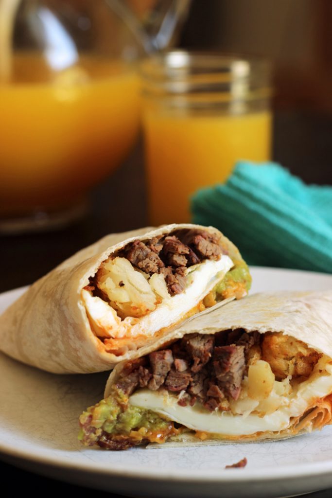 breakfast burrito cut in half, pitcher of orange juice