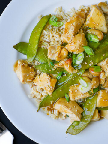 overhead shot of cashew chicken on a white dinner plate with a fork nearby on the black table.