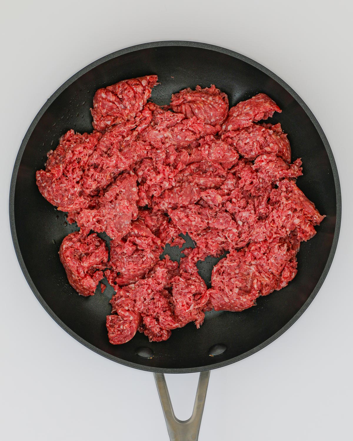 uncooked ground beef broken into chunks in a skillet.