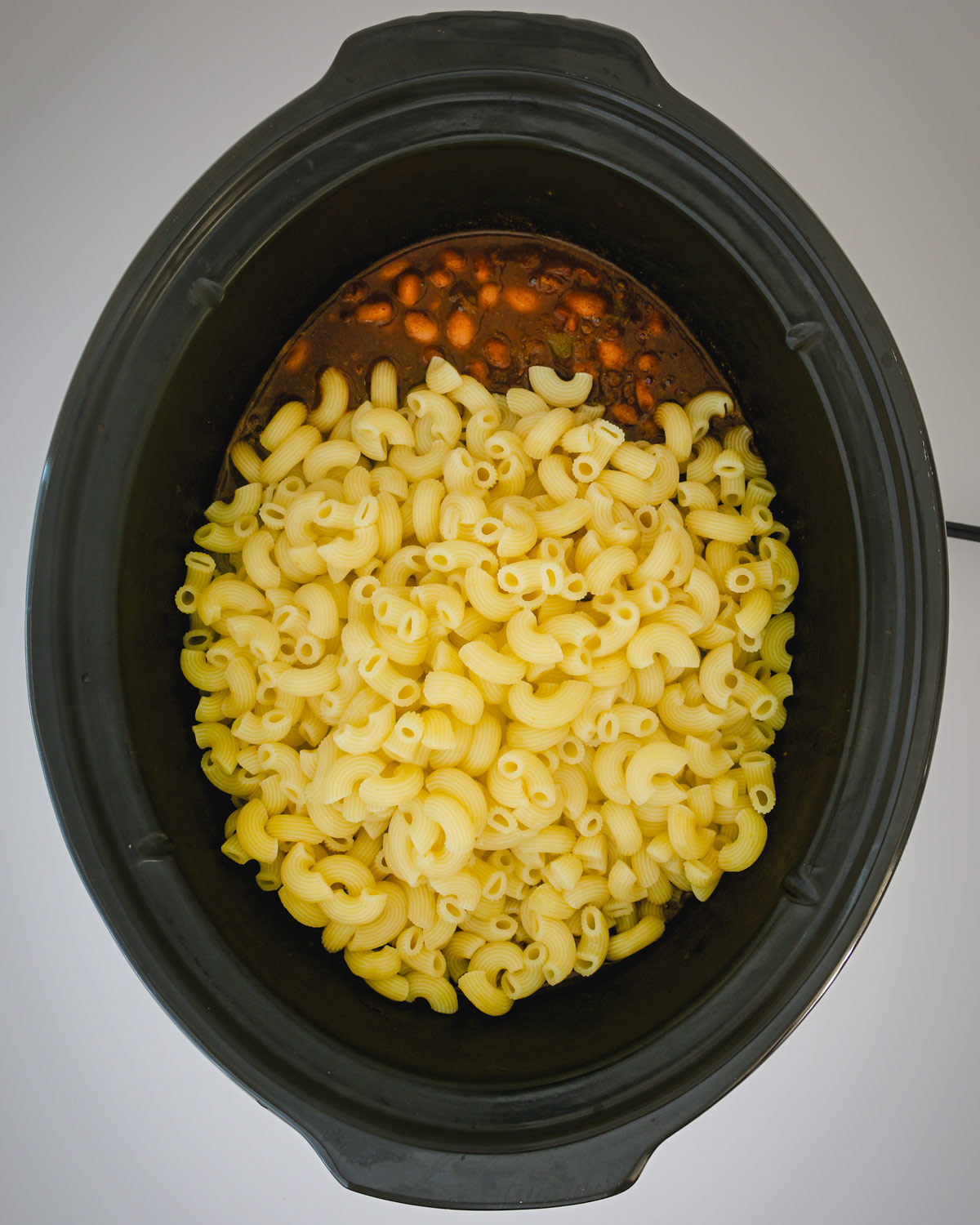 adding cooked macaroni to slow cooker chili.