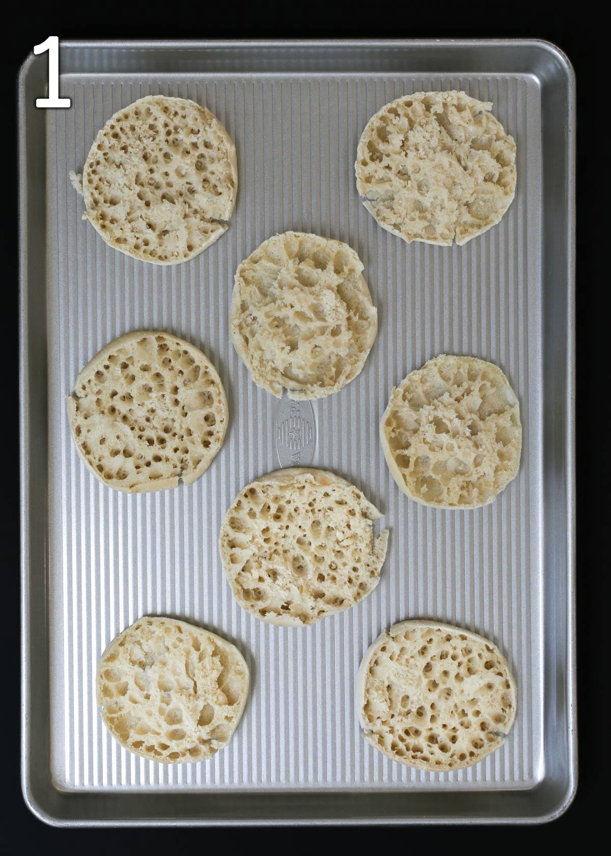 split english muffins laid out on baking sheet.