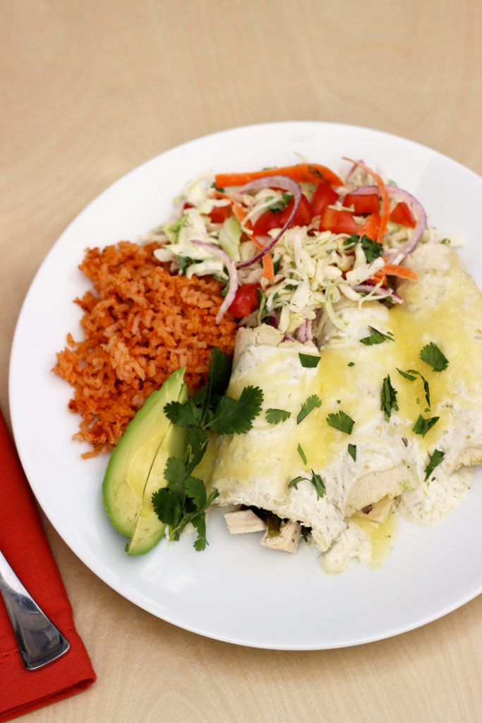 A plate of enchiladas with rice and vegetables