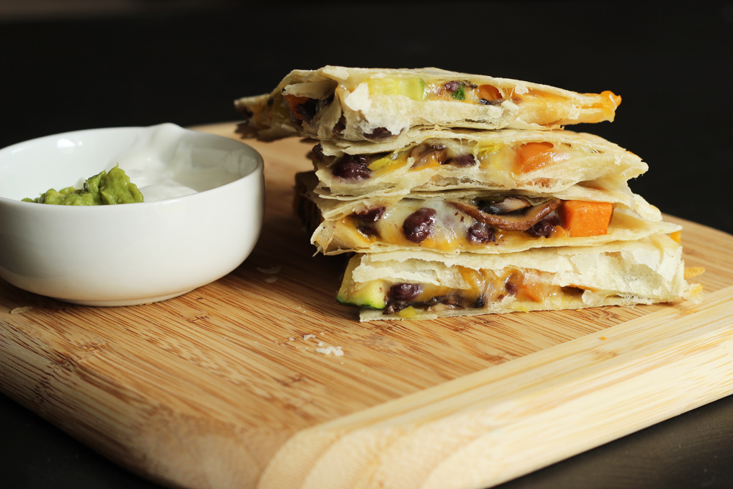 A quesadilla sitting on top of a wooden cutting board, with dish of sour cream