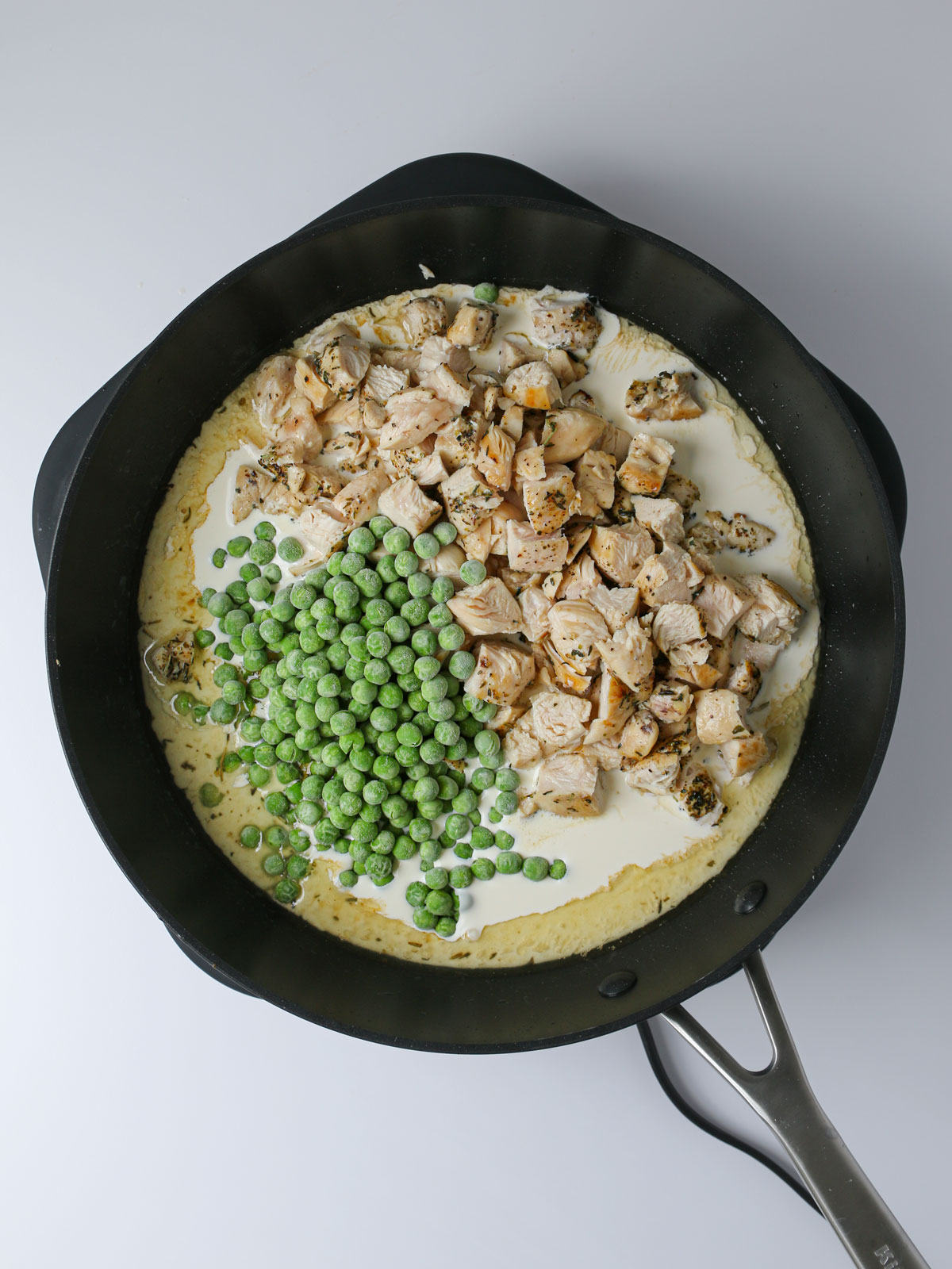 adding chicken, cream, and peas to the pan.