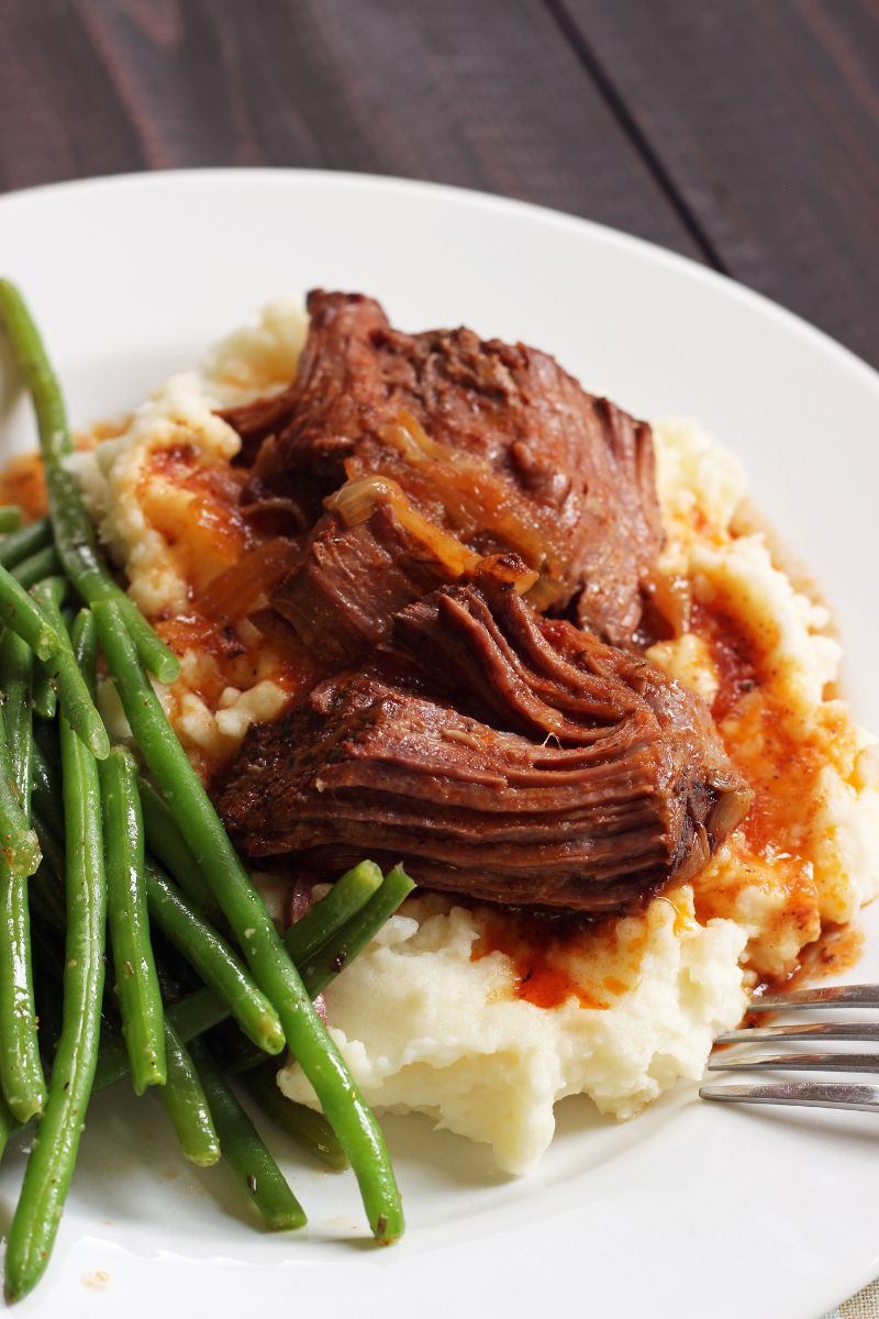 slow cooker pot roast on a bed of mashed potatoes with green beans on the side.