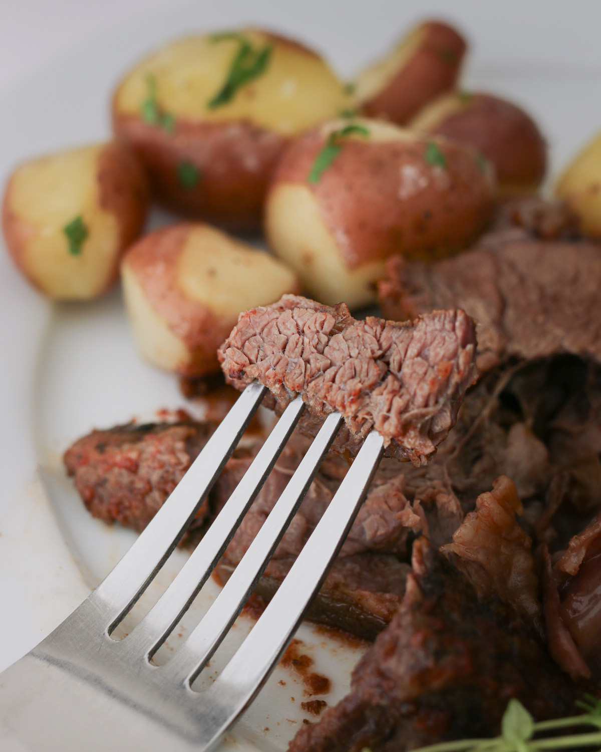 a forkful of pot roast in front of a plate of meat and potatoes.