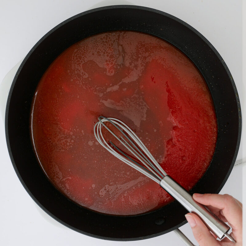 whisking together water and tomato sauce in skillet.