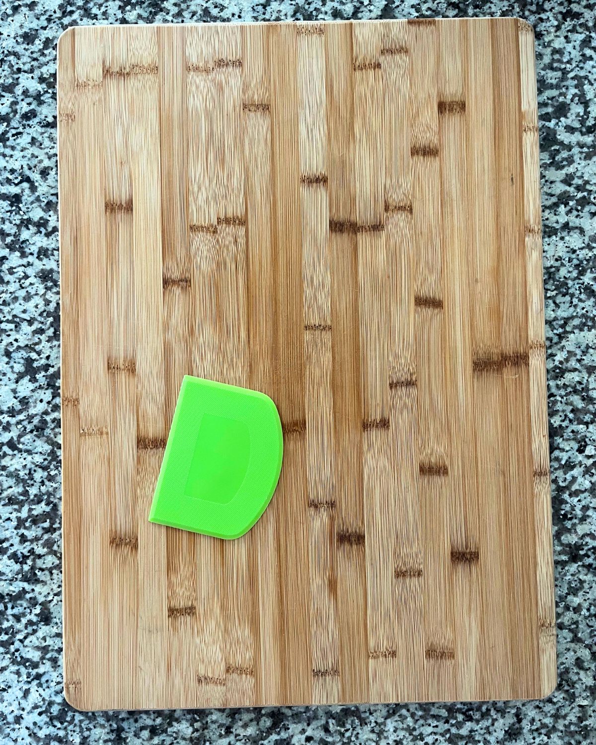 wooden cutting board and green rubber scraper on granite counter top.