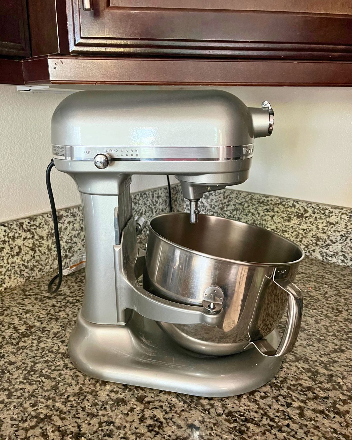 silver kitchen aid mixer on granite counter with dark wood overhead cabinet.