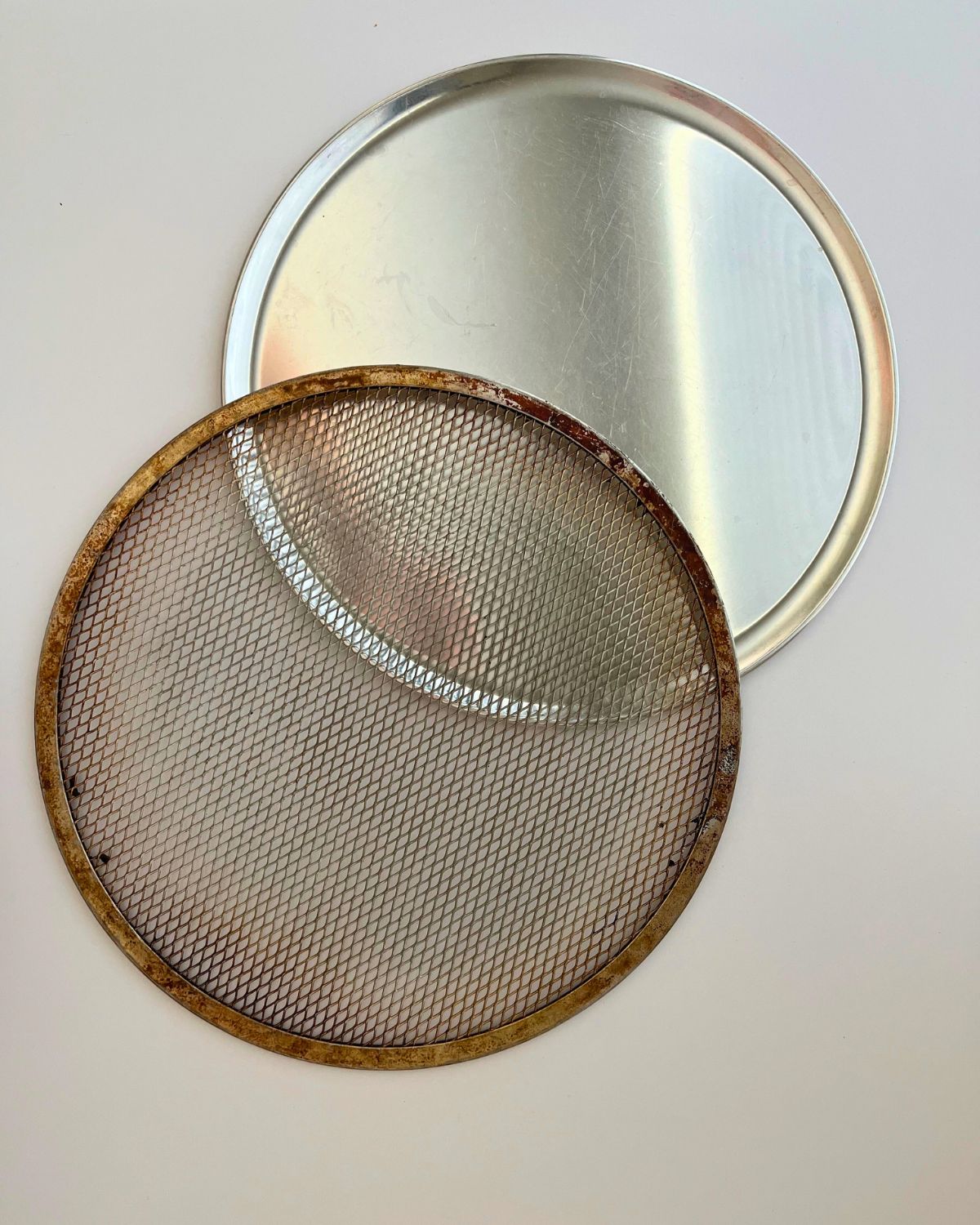 pizza screen and pizza pan on white counter.