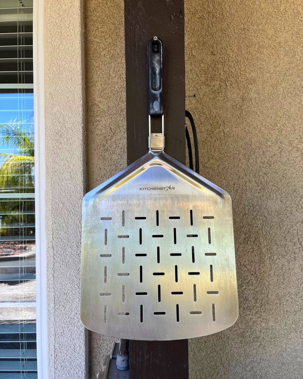 metal pizza peel hanging on nail outdoors.