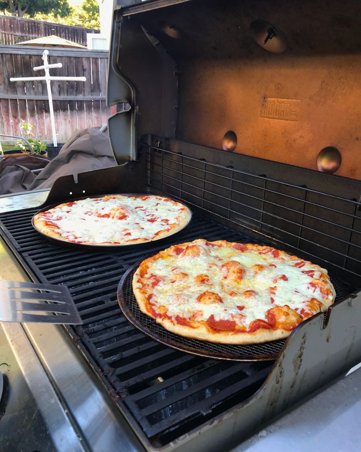 two pizzas on pizza screens on backyard grill.