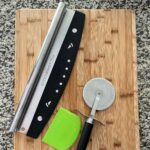 pizza tools: cutters and scraper on wooden cutting board.