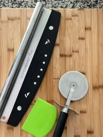pizza tools: cutters and scraper on wooden cutting board.