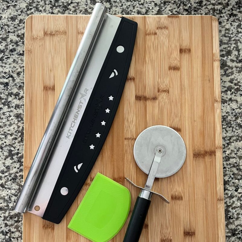 pizza tools: cutters and scraper on wooden cutting board.