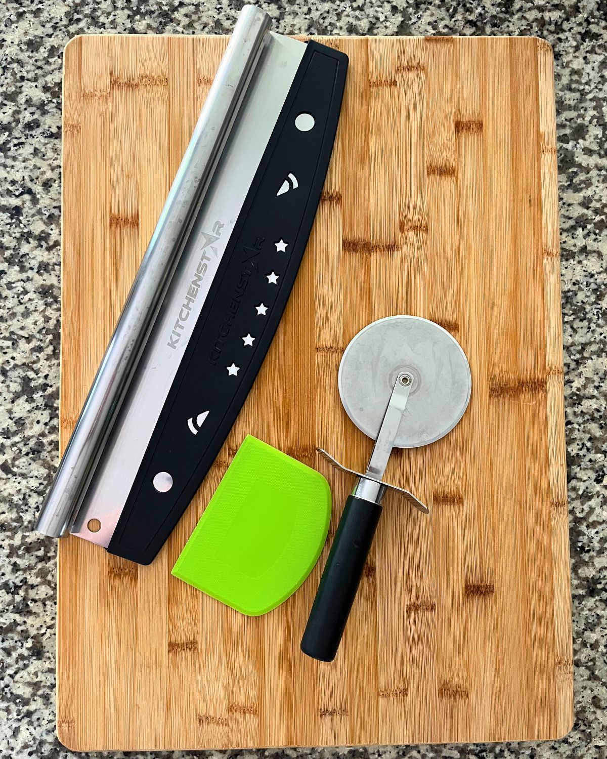 wooden board, two pizza cutters, and a dough scraper on granite counter top.