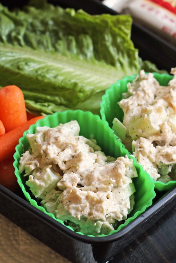 A close up of a plastic container of food, with Chicken Salad and veggies