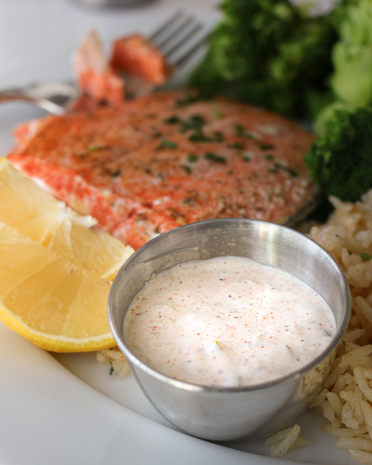 a dish of remoulade on a plate of salmon, rice, and broccoli.