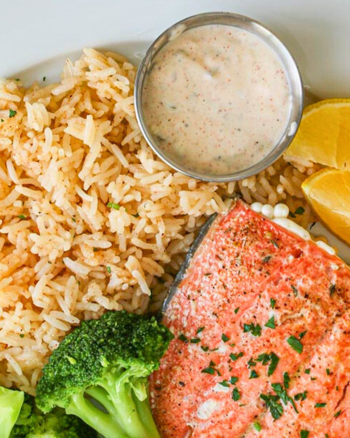 remoulade in a small silver cup on a plate of fish, rice, and veggies.